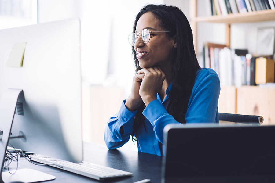 A smiling woman watching a webinar on her mac.